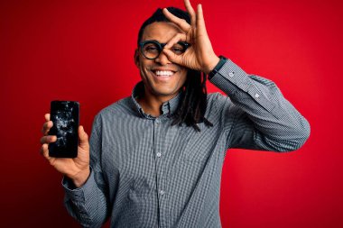 Kırık akıllı telefon tutan, gülümseyen bir ekran gösteren Afro-Amerikan genç adam el pençe divan duruyor.