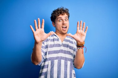 Kıvırcık saçlı, sıradan çizgili sweatshirt giyen, korku ifadesinden korkan genç, sarışın, yakışıklı bir adam. El kol hareketi yapmayı kes, şok içinde bağır. Panik konsepti.