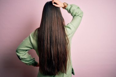 Pembe arka planda yeşil bir kazak giyen genç, güzel Asyalı kadın. Geriye doğru, elleri kafasında şüpheyi düşünüyor.