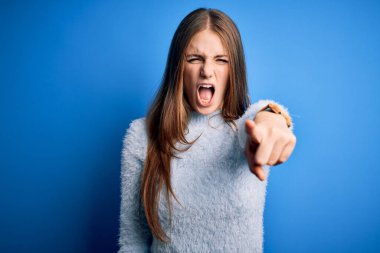 Genç, güzel, kızıl saçlı bir kadın, izole edilmiş mavi arka plan üzerine günlük süveter giyiyor. Kameraya kızgın ve sinirli olduğunu gösteriyor.