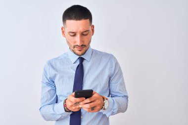 Genç yakışıklı iş adamı, izole edilmiş arka planda akıllı telefon kullanıyor. Akıllı bir yüz ifadesiyle ciddi olduğunu düşünüyor.