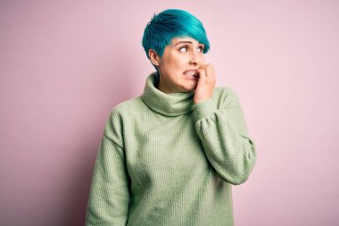 Mavi saçlı, balıkçı yaka kazak giyen genç ve güzel bir kadın gergin görünüyor ve elleri ağızdan tırnak yiyor. Endişe sorunu.