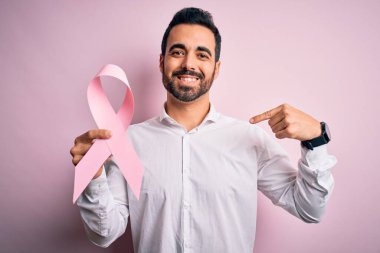 Sakallı, pembe kanser kurdelesini soyutlanmış arka planda tutan yakışıklı bir genç.