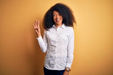 Afro saçlı, sarı arka planda duran ve dört numarayı işaret eden, kendinden emin ve mutlu gülümseyen güzel Afro-Amerikan zarif kadını..