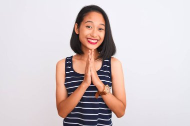 Çizgili tişört giyen genç Çinli bir kadın izole edilmiş beyaz arka planda durup ellerini birleştirip af diliyor kendinden emin bir şekilde gülümsüyor..