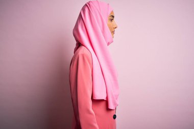 Pembe Müslüman başörtüsü ve iş ceketi giyen genç, güzel, esmer iş kadını. Taraf arıyor, rahat poz veriyor, kendine güvenen bir gülümseme takınıyor..
