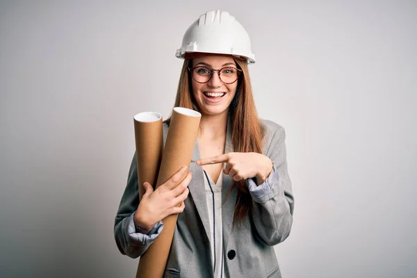 年轻美丽的红头发女建筑师 戴着眼镜 戴着安全帽 手里拿着设计图 手指手画脚 非常高兴 — 图库照片