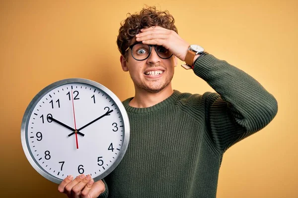 Młody Blondyn Kręconymi Włosami Okularach Trzymający Duży Zegar Żółtym Tle — Zdjęcie stockowe