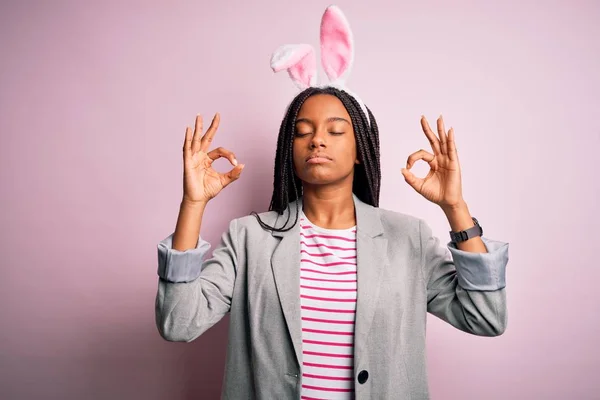 年轻的非洲裔美国女孩 戴着粉色背景的可爱的复活节兔子耳朵 闭上双眼微笑 用手指做冥想动作 瑜伽概念 — 图库照片