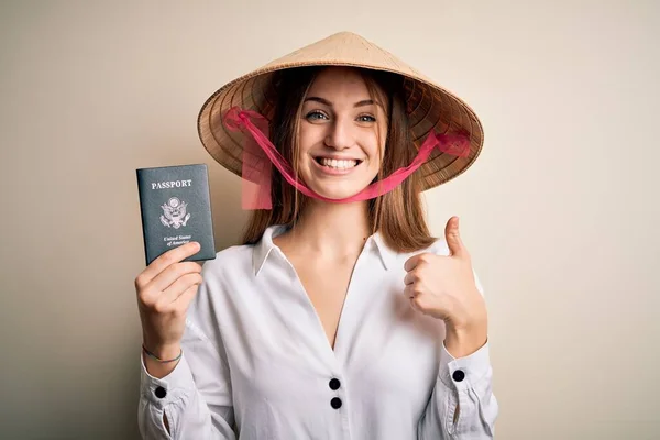アジアの伝統的な帽子をかぶって若い美しい赤毛の観光客の女性大きな笑顔で幸せなUsaパスポートを保持します — ストック写真