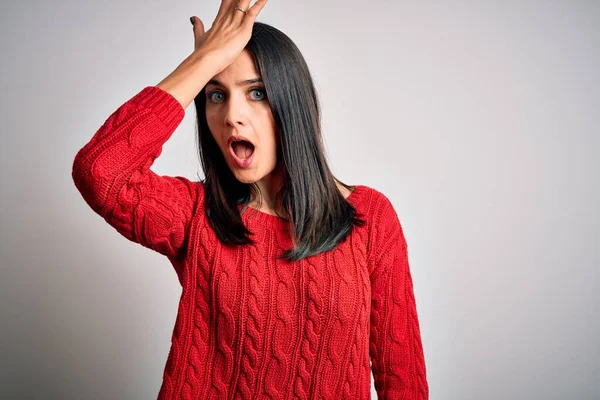 Young brunette woman with blue eyes wearing casual sweater over isolated white background surprised with hand on head for mistake, remember error. Forgot, bad memory concept.