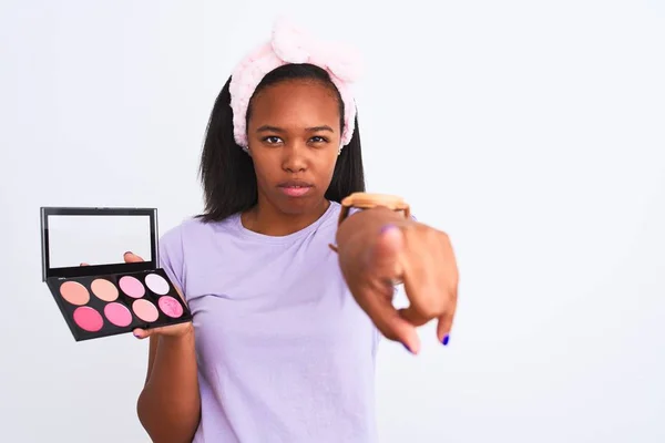 Young african american woman holding makeup palette over isolated background pointing with finger to the camera and to you, hand sign, positive and confident gesture from the front
