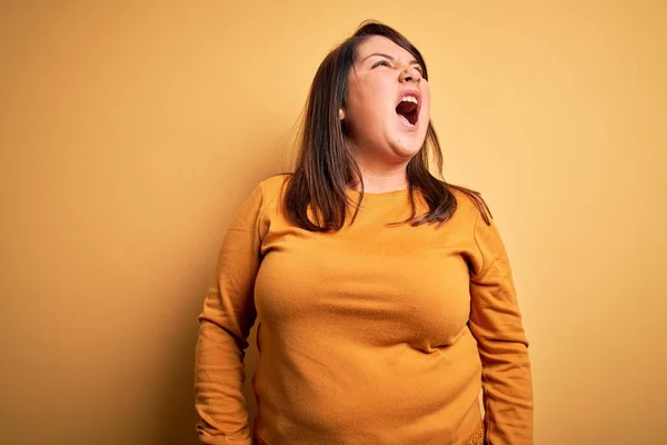 美しいブルネットプラスサイズの女性は怒りで叫んで 怒りで叫んで イライラし 激怒した孤立した黄色の背景にカジュアルなセーターを着ています 激怒と積極的な概念 — ストック写真