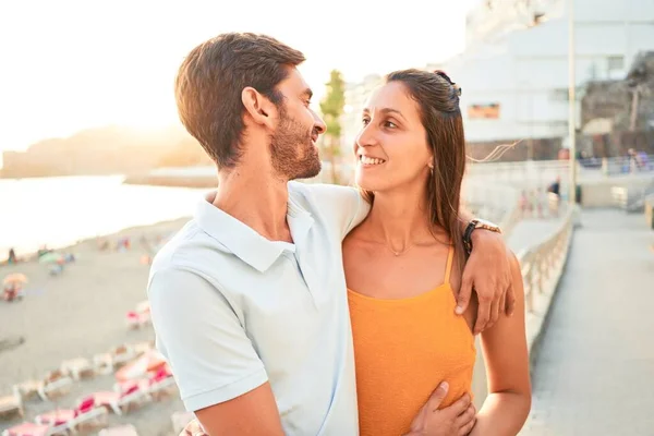 年轻漂亮的夫妇在度假时面带微笑 既快乐又自信 站在海滩上 面带微笑地拥抱着 — 图库照片