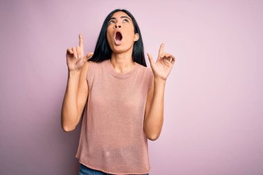 Pembe arka planda gündelik süveter giyen genç ve güzel İspanyol moda kadını şaşırmış ve şaşırmış bir şekilde başımı kaldırıp parmaklarımı ve kollarımı kaldırdım..