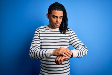 Rastgele çizgili kazak giyen, rahat ve kendinden emin genç, Afro-Amerikan Afro-Amerikan bir adam kol saatine bakıyor.