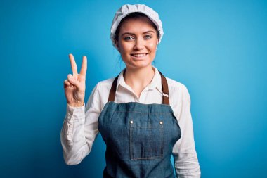 Mavi gözlü, mavi önlüklü, mavi arka planda şapkalı, gülümseyen, kameraya göz kırpan ve zafer işareti yapan genç, güzel fırıncı kadın. İki numara..