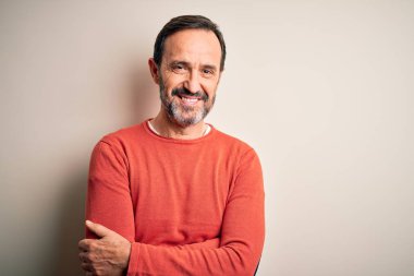 Orta yaşlı, turuncu süveter giyen, izole edilmiş beyaz arka planda duran, kollarını kavuşturup kameraya bakan, gülümseyen bir adam. Pozitif kişi.