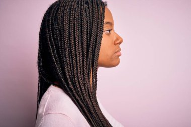Pembe süveter giyen genç Afro-Amerikan kadınlarını yakın çekim arka planda, yan yana bakan, rahat profil pozu veren, kendine güvenen bir gülümsemeyle doğal bir poz veren.