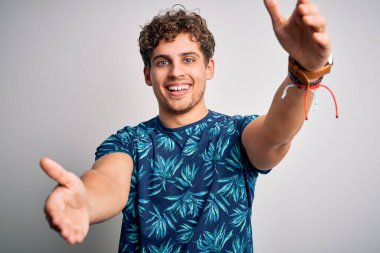 Sarışın, yakışıklı, tatilde. Kıvırcık saçlı, sıradan bir tişört giymiş. Kameraya bakıp kucaklaşmak için gülümsüyor. Mutluluğu kucaklayan neşeli bir ifade..