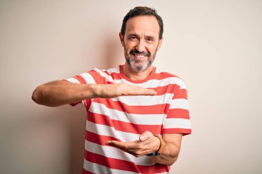 Orta yaşlı, beyaz tişörtlü bir adam izole edilmiş beyaz arka plan üzerinde duruyor. Ellerinde büyük ve büyük boy işareti, ölçü sembolü var. Kameraya bakıp gülümsüyor. Ölçüm konsepti.