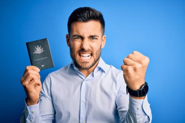 Avustralya pasaportu taşıyan genç, yakışıklı turist. Mavi arka planda. Sinirli ve sinirli. Öfkeyle bağırıyor.