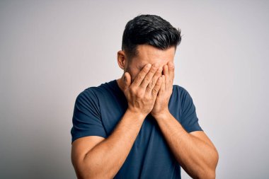 İzole edilmiş beyaz arka plan üzerinde duran sıradan tişört giyen genç yakışıklı bir adam. Ağlarken suratını ellerle kapatan üzgün bir ifade. Depresyon kavramı.