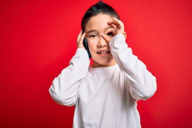 Küçük çocuk akıllı telefondan konuşuyor. Kırmızı izole edilmiş arka planda. Gülümsüyor.