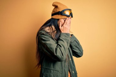 Kar gözlüğü takan ve kış havası için palto giyen genç ve güzel bir İspanyol kadın. Ağlarken yüzünü ellerle kapatan üzgün bir ifade. Depresyon kavramı.