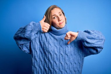 Mavi arka planda balıkçı yaka kazak giyen genç, güzel sarışın bir kadın. Baş parmaklarını yukarı aşağı hareket ettiriyor. Anlaşmazlık ve uzlaşma ifadesi. Çılgın çatışma