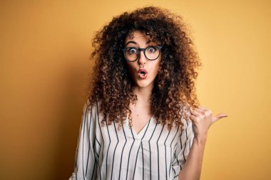 Kıvırcık saçlı, piercingli, çizgili tişörtlü ve gözlüklü genç ve güzel bir kadın..