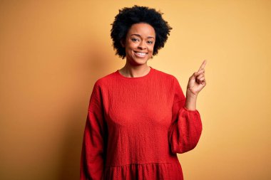 Kıvırcık saçlı, yüzünde kocaman bir gülümseme olan, elleri ve parmaklarıyla kameraya bakan Afro-Amerikan bir kadın..