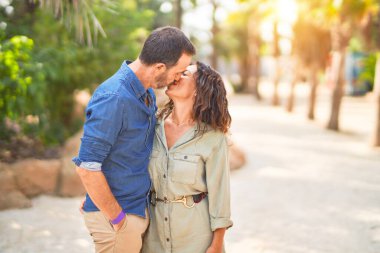 Şehir parkında mutlu ve kendinden emin gülümseyen orta yaşlı güzel bir çift. Yüzünde gülümsemeyle ayakta durup sarılıp öpüşmek.