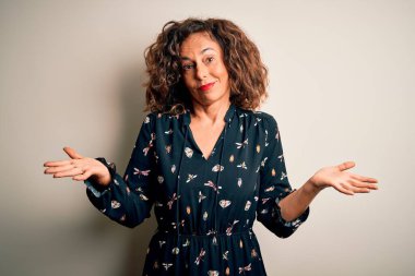 Orta yaşlı, güzel bir kadın izole edilmiş beyaz arka planda dikilmiş kolları ve elleri havada, kafası karışmış bir şekilde duruyor. Şüphe kavramı.