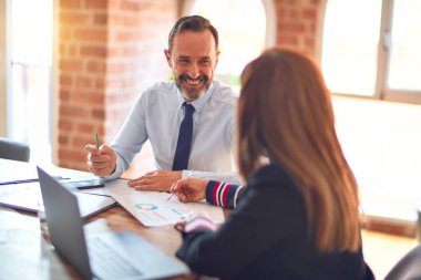 Mutlu ve kendinden emin gülümseyen iki orta yaşlı iş adamı. Ofiste dizüstü bilgisayarla gülümseyerek birlikte çalışıyoruz.