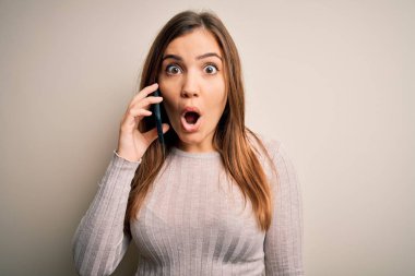 Akıllı telefondan konuşan genç bir kadın izole edilmiş bir arka planda şaşkınlık dolu bir yüzle korkmuş ve korku ifadesinden korkan bir kadın.