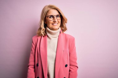 Orta yaşlı güzel sarışın iş kadını zarif pembe ceket giyiyor ve yüzünde mutlu ve havalı bir gülümseme olan gözlük takıyor. Şanslı kişi..