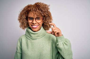 Güzel Afro-Amerikan kadın balıkçı yaka kazak ve gözlük takıyor gülümsüyor ve kendine güvenen el hareketleriyle küçük beden işareti yapıyor parmaklarıyla ve kamerayla bakıyor. Ölçü kavramı.