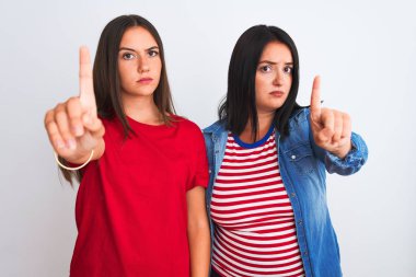 İzole edilmiş beyaz arka planda dikilen, rahat kıyafetler giyen genç ve güzel kadınlar. Parmağını kaldırmış ve kızgın bir ifadeyle işaret ediyorlar.