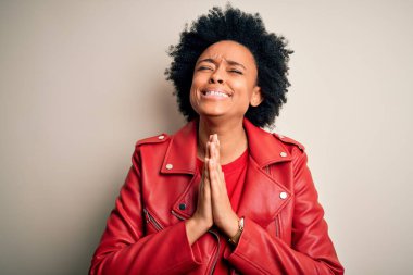 Kıvırcık saçlı, genç, Afro-Amerikan bir kadın. Sıradan kırmızı bir ceket giyiyor. Elleri bağlı yalvarıyor ve dua ediyor. Yalvarıyorum..