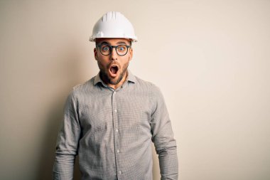 İzole edilmiş arka planda miğfer takan genç mimar şaşırmış, korkmuş ve şaşırmış bir ifade, korku ve heyecanlı bir yüz takınıyor..
