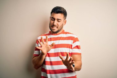 İzole edilmiş beyaz arka plan üzerinde duran sıradan çizgili tişört giyen genç yakışıklı adam tiksindirici ve tiksindirici bir yüz ifadesi takınıyor çünkü iğrenme reaksiyonu yüzünden tiksinti ifadesi takınıyor..