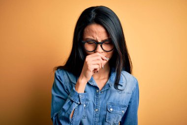 İzole edilmiş sarı arka plan üzerinde sıradan kot gömlek giyen genç ve güzel Çinli kadın kendini iyi hissetmiyor ve soğuk algınlığı veya bronşitin belirtisi olarak öksürüyor. Sağlık hizmeti kavramı.