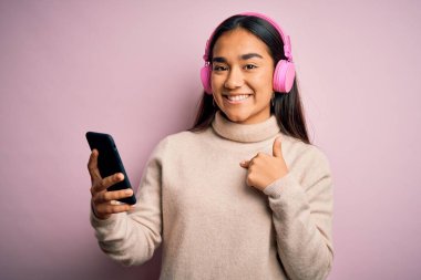 Genç, güzel Asyalı bir kadın akıllı telefon ve kulaklık kullanarak müzik dinliyor.