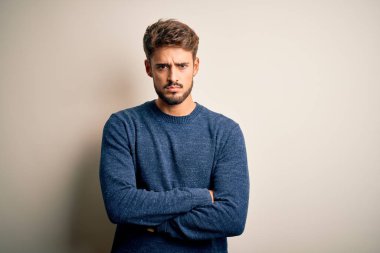 Sakallı, sıradan süveter giyen, beyaz arka planda duran, kuşkucu ve gergin, yüzünde çapraz kollu tasvip etmeyen genç yakışıklı bir adam. Negatif kişi.