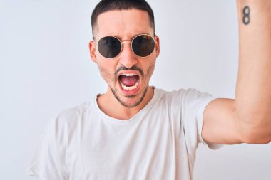 Güneş gözlüğü takan genç yakışıklı bir adam ve izole edilmiş arka planda rahat bir tişört. Sinirli ve sinirli bir şekilde bağırıyor, çıldırıyor ve bağırıyor.
