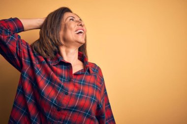 Orta yaşlı, güzel bir kadın izole edilmiş sarı arka planda dikilmiş kendine güvenen, el hareketleriyle saçlara dokunan çekici ve şık poz veren bir kadın.
