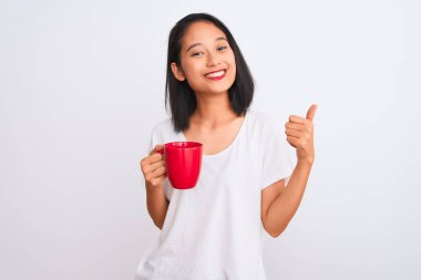 Genç, güzel Çinli bir kadın izole edilmiş beyaz arka planda bir fincan kahve içiyor. Kocaman gülümsüyor. İşaret veriyor.