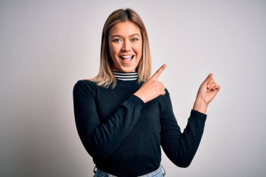 Genç, sarışın, mavi gözlü, beyaz, soyutlanmış arka planda duran, gülümseyen ve kameraya bakan iki eliyle ve parmaklarıyla yüzünü gösteren bir kadın..