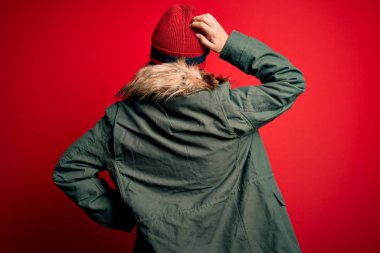 Kayak gözlüğü takan genç sarışın kız ve kırmızı arka planda kayak yapmak için kışlık palto giyen kız. Elleri başının üstünde şüpheyi düşünüyor.